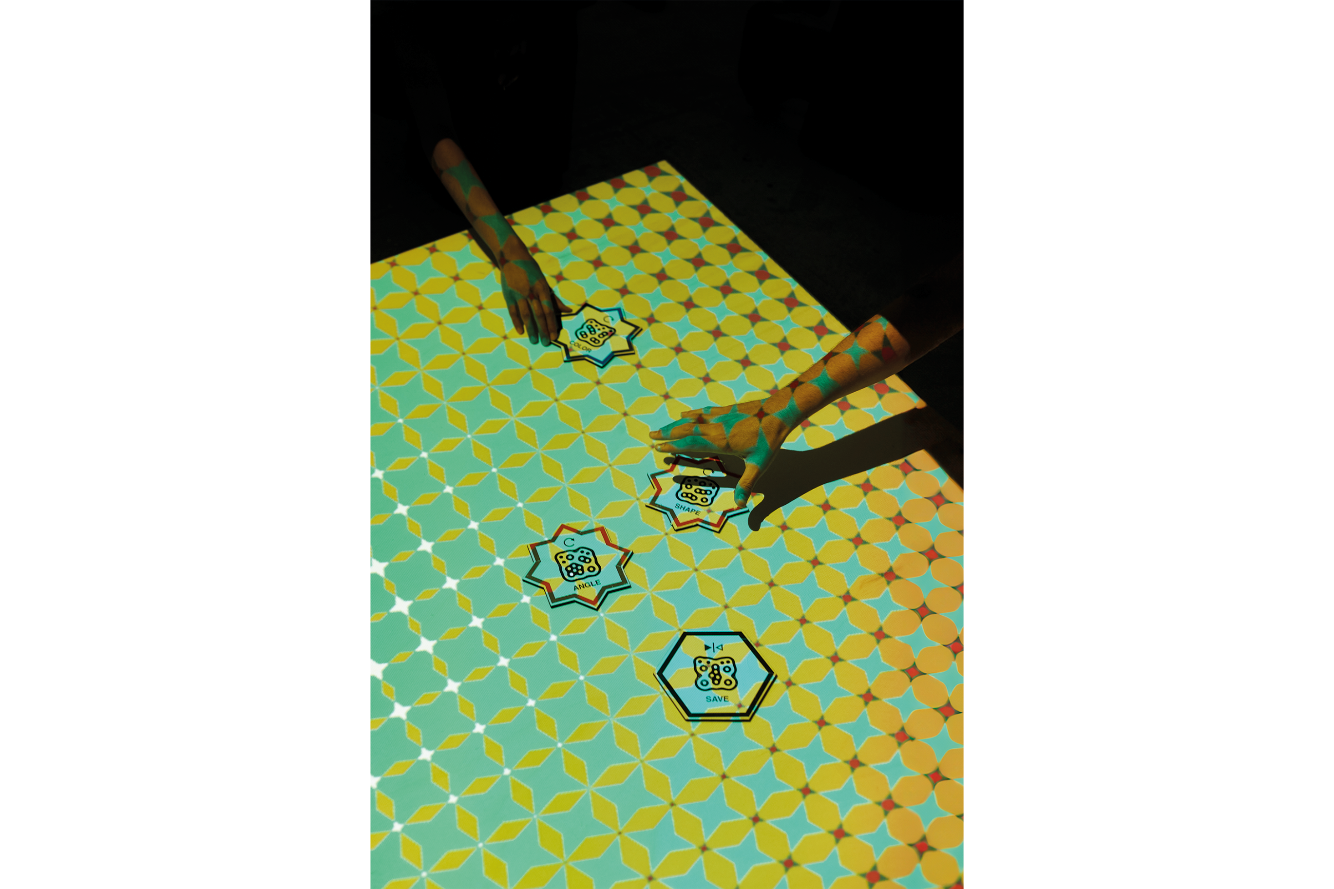 Two hands interacting with markers on a colourful projected pattern