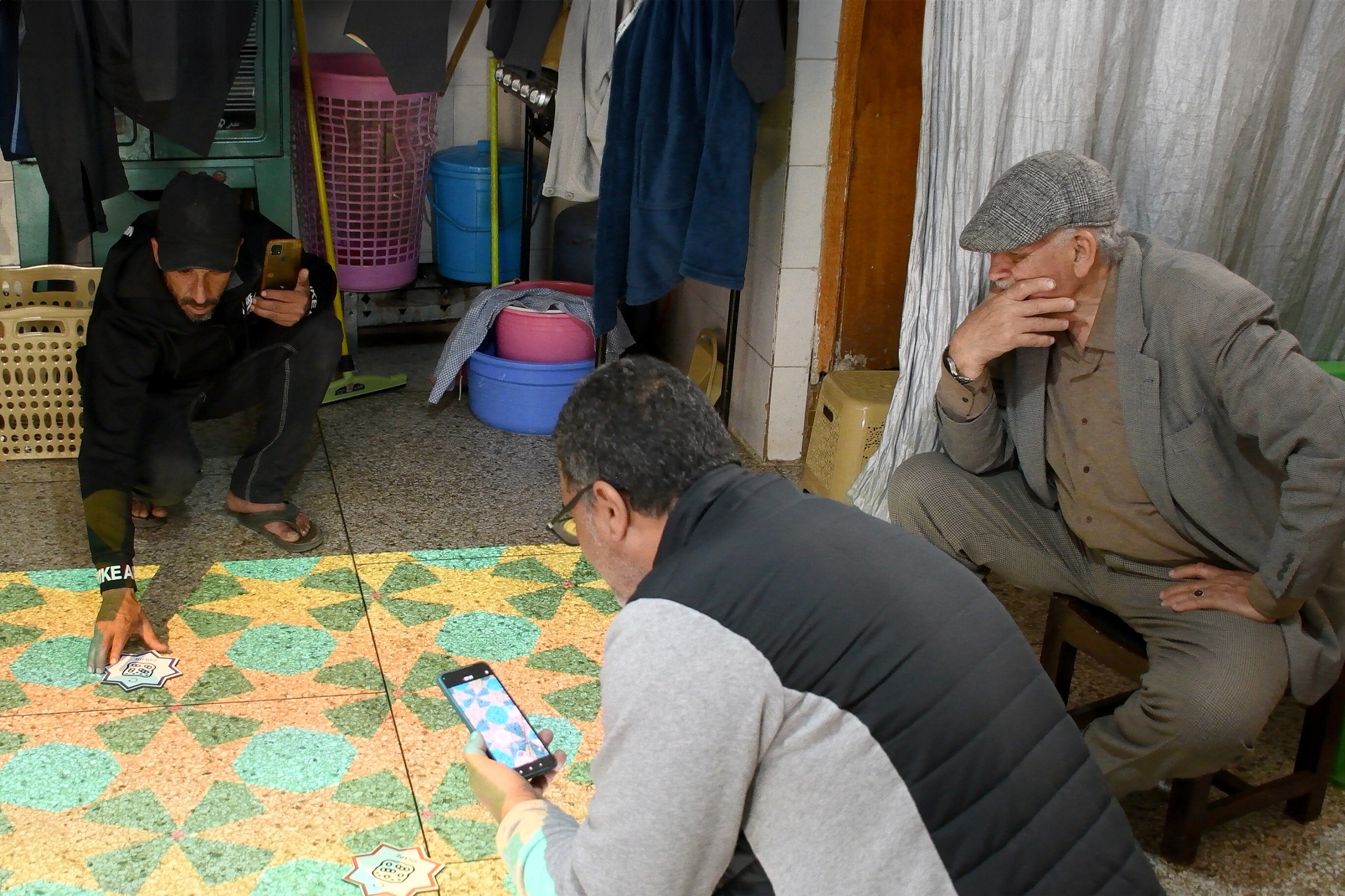 Three moroccan craftsmen kneeling to interact with markers on the floor.