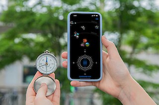 Person holding a compass in their left hand, and a smartphone with the Ody-C application in their right hand