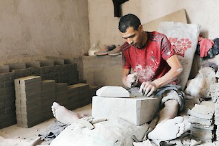 One moroccan craftsman sitting on the floor and cutting tiles out of unfired clay.